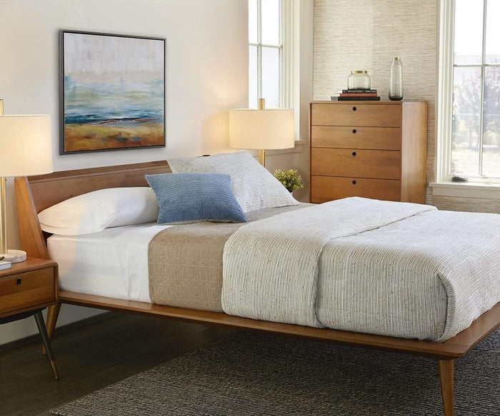A neatly made bed with neutral bedding, a wood headboard, blue accent pillow, two lamps, a tall wooden dresser, the Lanson Nightstand in mid-century style, and abstract art on the wall in a bright, modern bedroom.