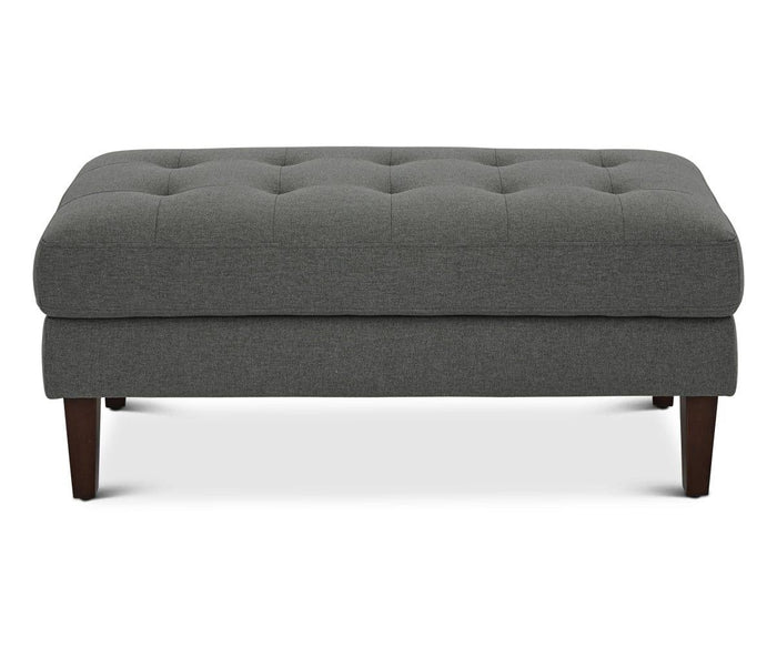 The Laura Ottoman in Grey B-1009 is a rectangular, modern piece featuring button tufting on top and four dark wooden legs, displayed against a white background.