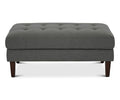 The Laura Ottoman in Grey B-1009 is a rectangular, modern piece featuring button tufting on top and four dark wooden legs, displayed against a white background.