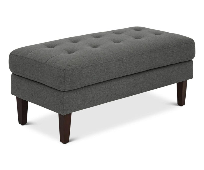 Introducing the Laura Ottoman: a rectangular, dark gray ottoman featuring button tufting on its upholstered top and supported by four dark wooden legs. This modern piece is showcased against a plain white background.