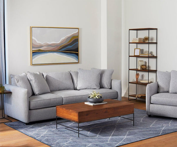 A modern living room with a gray sofa, the Leende C-Table crafted from European oak, a geometric rug, abstract wall art, and a metal-framed shelf with decor items exudes a subtle rustic-industrial design charm.