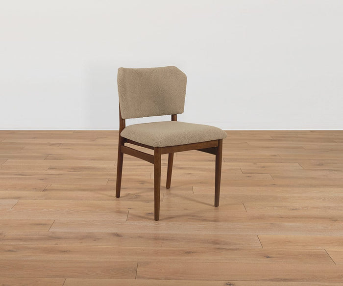 The Leevi Dining Chair, crafted from solid rubberwood and featuring a cushioned beige seat and backrest upholstered in performance fabric, is positioned on a light brown wooden floor with a plain white wall backdrop.