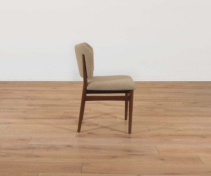 The Leevi Dining Chair, crafted from wood and featuring a beige cushioned seat and backrest upholstered in performance fabric, is displayed in a side view on a light wood floor with a plain white wall background.