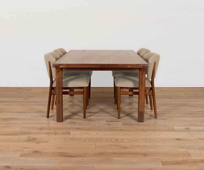 A wooden dining table with four Leevi Dining Chairs—each expertly crafted from solid rubberwood and upholstered in performance fabric—sits on a light wood floor against a plain white wall.