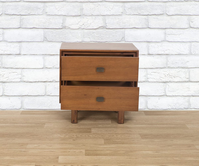 The Leevi Nightstand, crafted from wood, features two drawers—both shown partially open. This mid-century piece is accented with square metal handles and stands on four short legs. The scene is set against a white brick wall and a wooden floor.