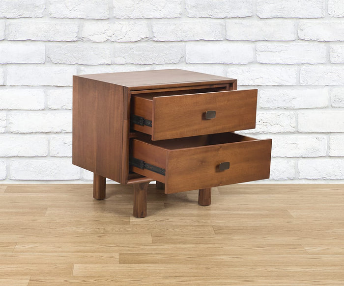 A Leevi Nightstand with its two drawers open, made from solid acacia wood, stands on a light wood floor set against a white brick wall.