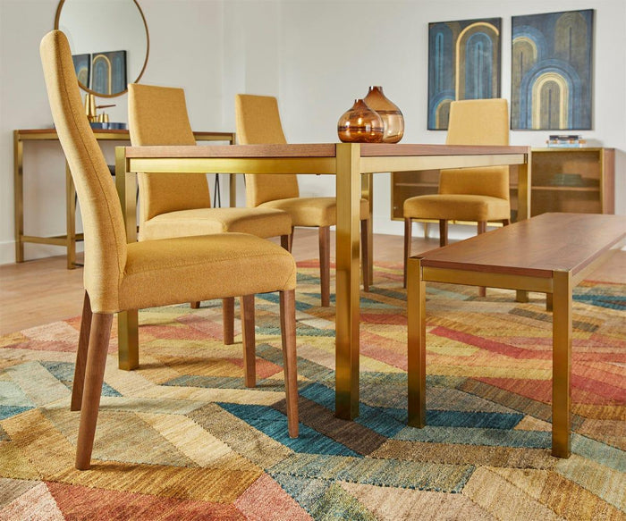 Contemporary dining room featuring Lussa Fabric Dining Chairs with solid wood legs and plush upholstery, paired with a wooden dining table accented by gold legs, a coordinating bench, geometric rug, abstract wall art, a console table, and a round mirror. Warm tones and vibrant colors create a modern atmosphere.