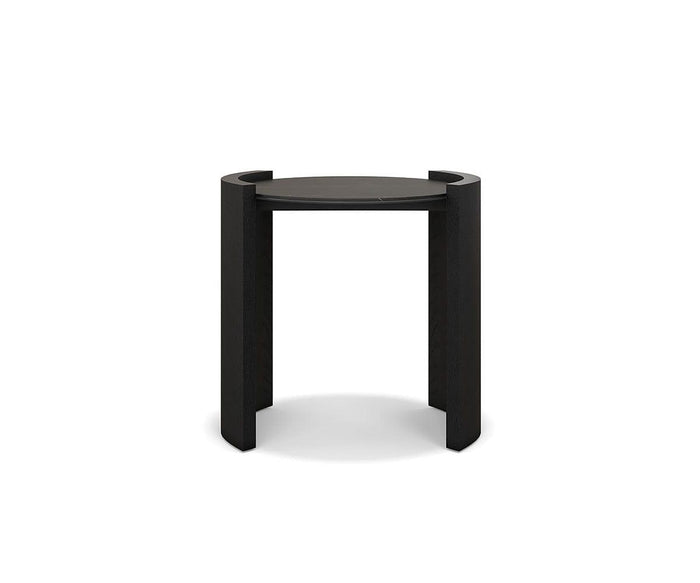 The Matteo Round End Table in Black Oak/Ceramic features a modern round top supported by three straight legs that extend just above the surface, creating partial circular handles on each side. Crafted with a minimalist and contemporary design, this solid oak end table brings a sophisticated touch to any space.
