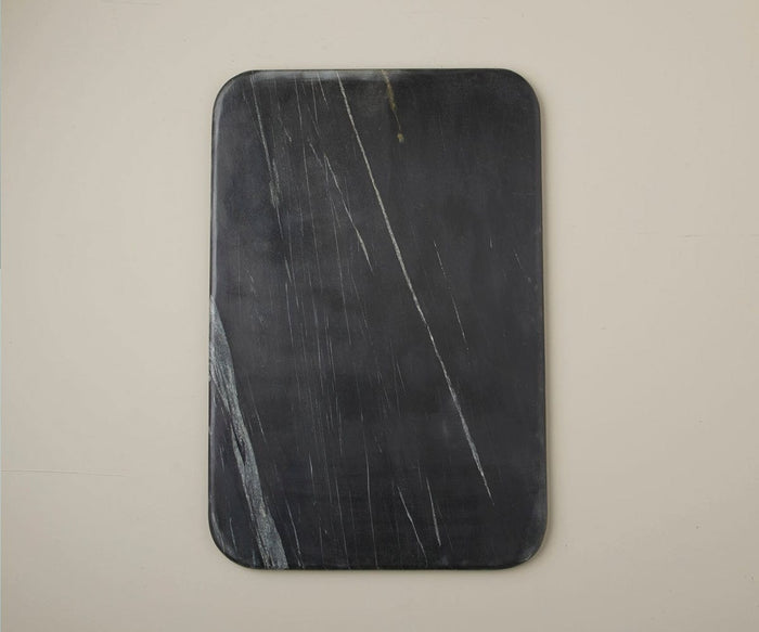 The Mirco Black Marble Slab, featuring a handcrafted design with rounded corners and delicate white streaks, sits against a plain beige wall, adding an elegant touch of decor to the space.