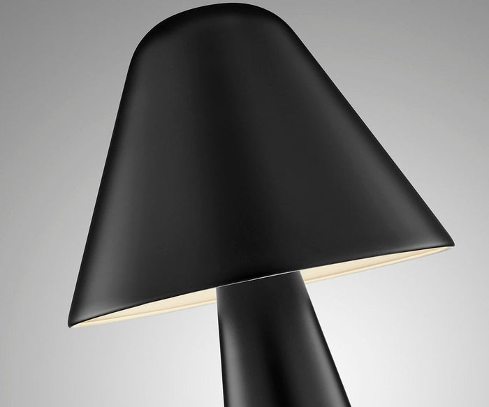 Close-up of the Muga Table Lamp, featuring a sleek, modern design with a wide conical black metal shade, softly illuminated at the edges and set against a plain gray background.