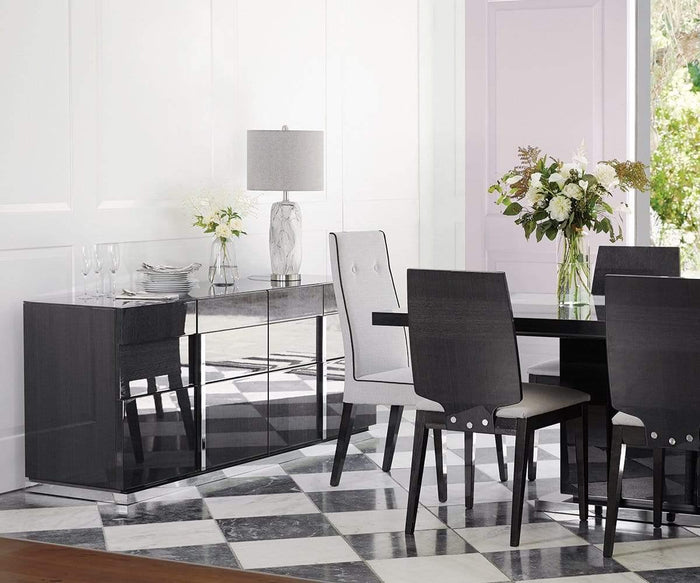 Modern dining room with a black table, four gray cushioned chairs, and a sideboard with mirrored doors. The sideboard is topped with the Nemling Table Lamp, which features a ceramic body and linen drum shade, alongside flowers and tableware. The floor displays a black and white checkerboard pattern.