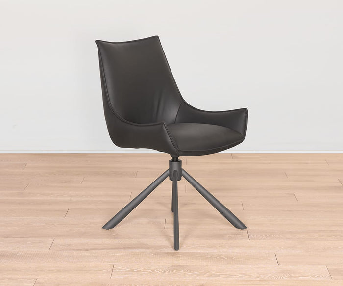 The Nomi Dining Chair is a modern black swivel chair with a curved backrest and four angled metal legs, featuring a sleek faux leather seat. It is shown placed on a light wood floor against a plain white wall.