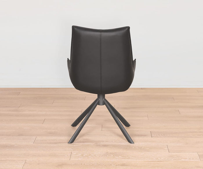 The Nomi Dining Chair, featuring a modern design with a black faux leather seat and four angled legs, is displayed from the back on a light wooden floor against a plain white wall.