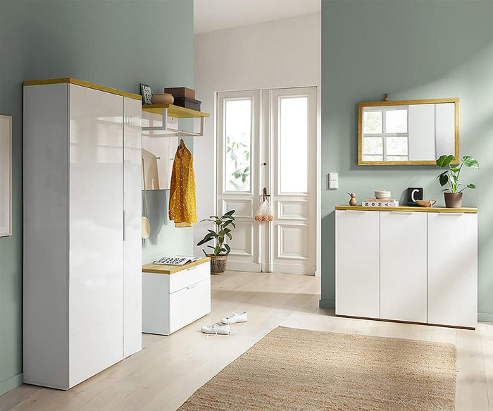 Modern entryway featuring white cabinets, the eco-friendly Oakley Entryway Bench with coat hooks, a spacious wardrobe, a mirror above a sideboard, and a potted plant. Sunlight pours through glass double doors, while shoes and a bag rest on the floor—highlighting thoughtful home organization.