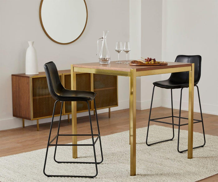 A modern dining area features a square wooden table paired with two sleek Oken Bar Stools, wine glasses, a wine decanter, and a cheese plate. A mirror and vase sit elegantly on a sideboard against a crisp white wall.