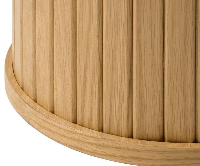 Close-up of the Orella Round Coffee Table—a cylindrical wooden piece featuring vertical grooves and a rounded base, with light wood grain and a smooth, polished texture reminiscent of tambour paneling commonly found in modern living room décor.