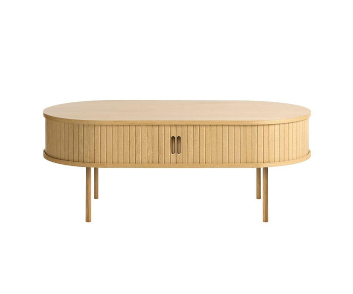 The Orella Storage Coffee Table in natural oak veneer features an oval shape with vertical slat tambour paneling, four slender legs, and two central cabinet doors for storage. Shown against a white background, it offers an elegant addition to any modern living room.