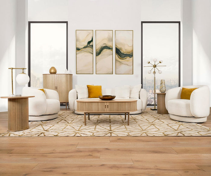 Modern living room with white, rounded furniture, gold accents, abstract wall art, and large windows showing a city view. Light wood floors and a geometric rug complete the stylish, airy space, while the Aerlig Table Lamp adds both function and flair to the decor.