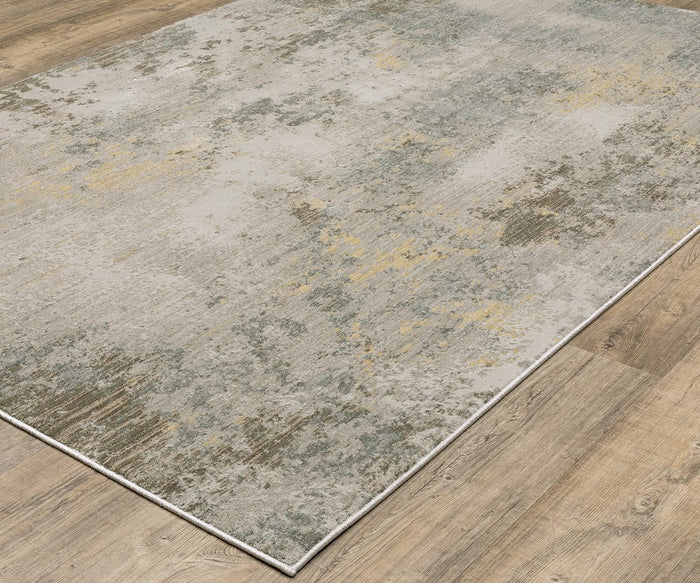 The Oriental Weaver Mallory / MAL02 Rug is a modern, power-loomed piece featuring a distressed, abstract pattern in shades of beige, gray, and muted gold set against a light wooden floor. Crafted from space dyed polypropylene, this rug showcases an organic design that offers both contemporary style and lasting durability.