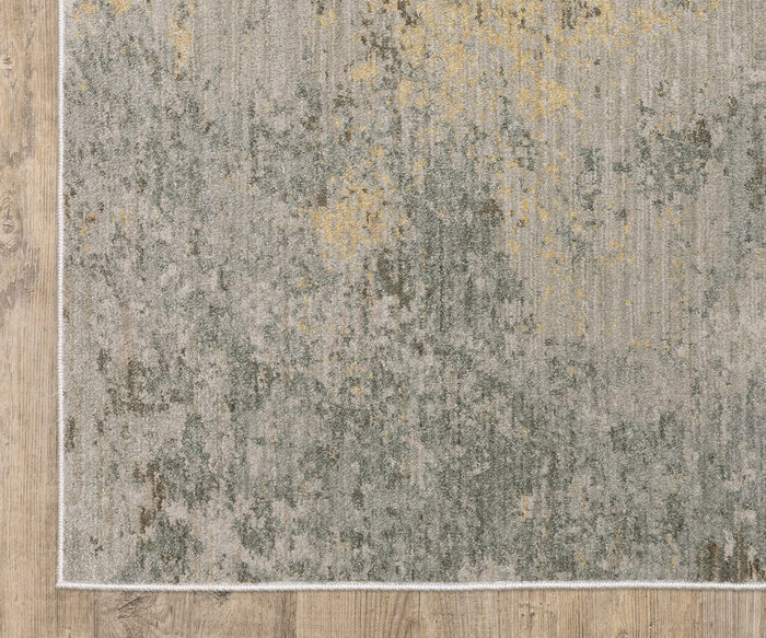 A close-up of the Oriental Weaver Mallory / MAL02 Rug, a rectangular power-loomed piece crafted from space-dyed polypropylene, showcases its distressed organic pattern in shades of gray, green, and yellow. The rug is placed on a light wood floor and finished with a thin white border.