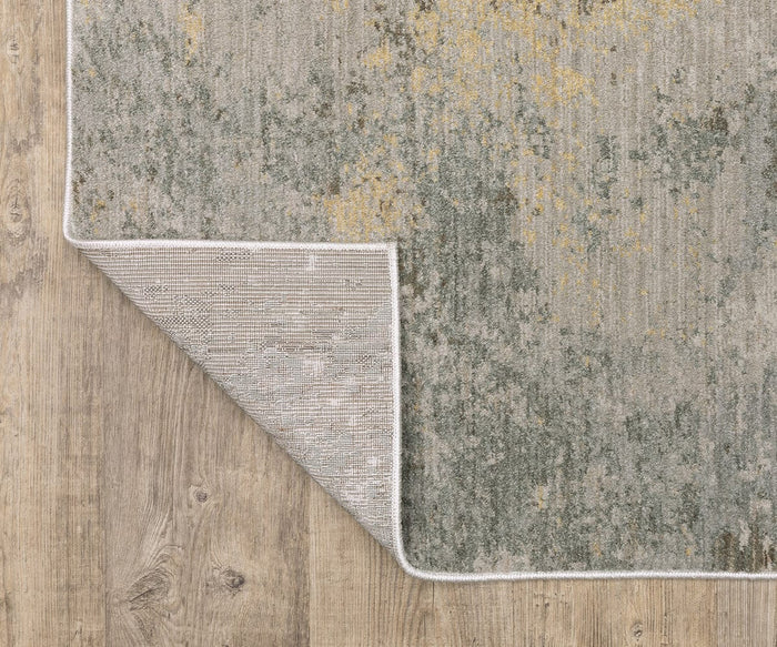 The Oriental Weaver Mallory / MAL02 Rug, a neutral-toned power-loomed piece featuring subtle green and gold patterns, is displayed on a wooden floor with one corner flipped to showcase its space-dyed polypropylene weaving and organic pattern design.
