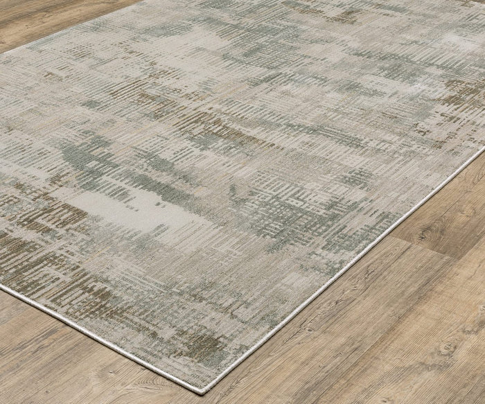 The Oriental Weaver Mallory / MAL03 Rug is a rectangular, power-loomed rug featuring a modern abstract pattern in muted tones of gray, beige, and green. Crafted from space dyed polypropylene, it is pictured here on a light wood floor.