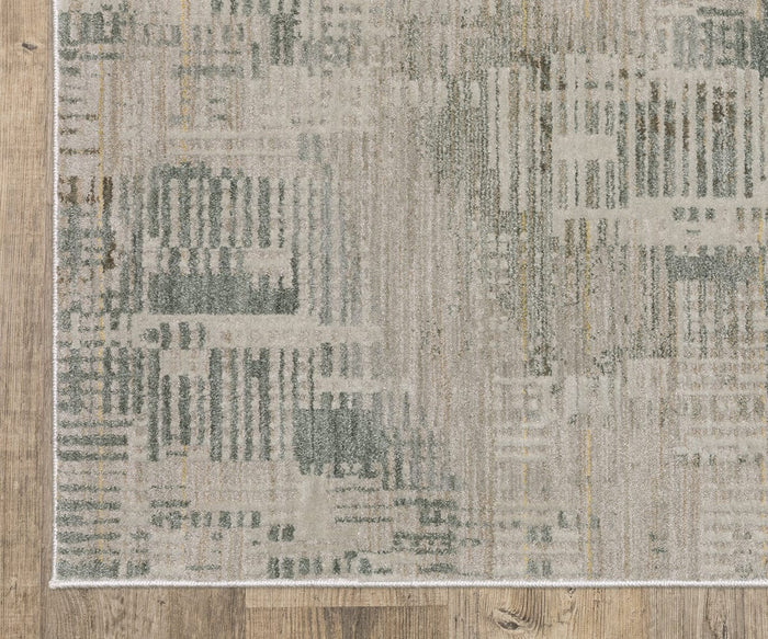 The corner of the Oriental Weaver Mallory / MAL03 Rug is shown on a light brown wood floor, displaying its patterned design in shades of gray and beige with geometric and linear motifs. This power-loomed area rug is crafted from space dyed polypropylene for added durability, though only part of the rug and the floor are visible.