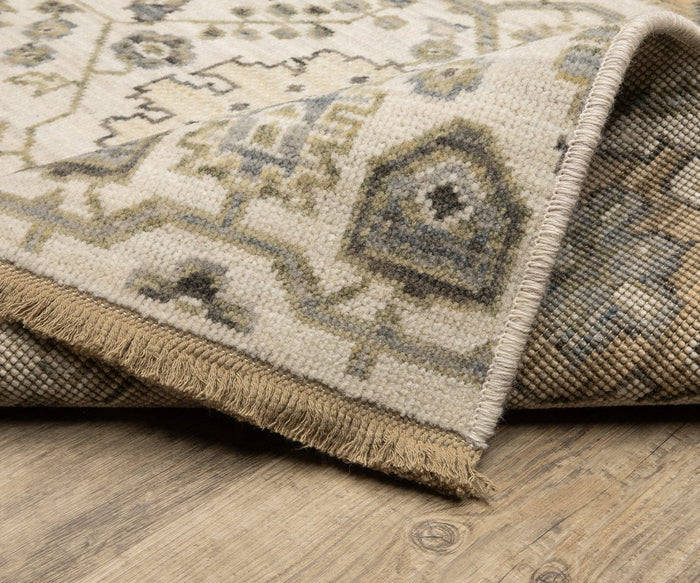 A corner of the Oriental Weavers Acacia / ACA11 Rug in beige and gray is folded over to reveal the backside. Placed on a wooden floor, this rug features fringed edges and geometric patterns, bringing a subtle boho vibe to the space.