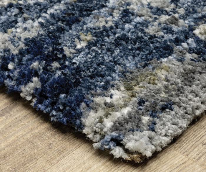 A close-up of the Oriental Weavers Aspen / 2061L Rug, crafted from space-dyed microfiber polyester and featuring an abstract design in multicolored shades of blue, gray, and white, displayed on a light wooden floor.