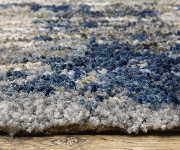Close-up of the Oriental Weavers Aspen / 2061L Rug, an abstract design crafted from space-dyed microfiber polyester, showcasing plush, textured shades of blue, gray, and cream on a wooden floor.
