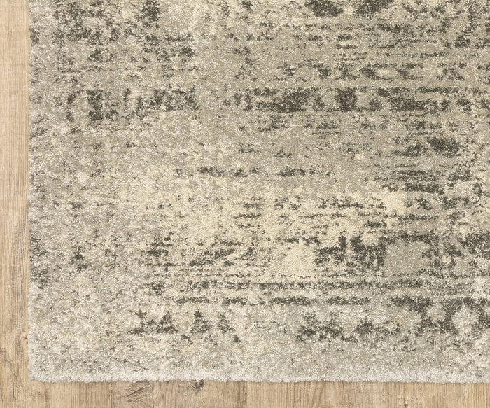 A close-up of the corner of the Oriental Weavers Astor / 1806Q Rug, featuring its plush pile and distressed gray and cream pattern with vintage-inspired motifs, displayed on a wooden floor.