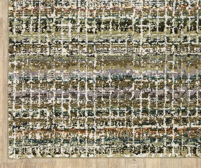 A close-up of the Oriental Weavers Atlas / 747A Rug, a machine-woven piece from the Atlas Collection, showcasing its textured surface and abstract multicolored design in green, white, brown, and purple hues on a light wooden floor—an ideal choice for high-traffic areas.
