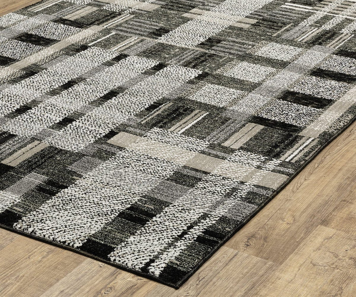 The Oriental Weavers Atlas / 752C Rug, a modern machine-woven piece from the Atlas Collection, showcases a black, gray, and white geometric pattern with various rectangles and textured designs. Placed on a light wood floor, this contemporary rug is ideal for high-traffic areas.
