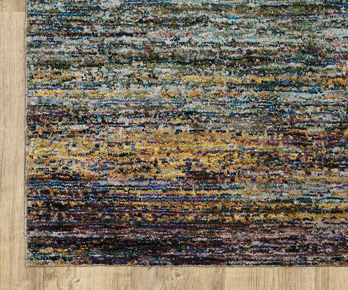 A closeup of the Oriental Weavers Atlas / 8037B Rug, featuring colorful, textured abstract patterns in yellow, blue, and gray tones, displayed on a light wood floor; this durable area rug is expertly machine-woven for lasting style and performance.