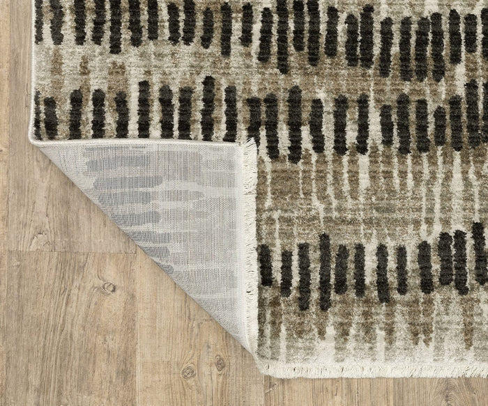 A corner of the Oriental Weavers Bauer / 8120D Rug is folded over, exposing the underside. Crafted from recycled PET yarn, this rug showcases a brown, beige, and black abstract design and rests on a light wood floor.