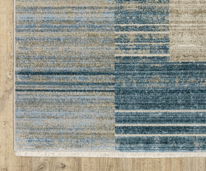 A close-up of the Oriental Weavers Bauer / 90B Rug, featuring blue, beige, and gray rectangular patterns on a light wooden floor. The rug’s fringed edges are visible at the bottom, and its recycled PET yarn construction makes it easy to clean.