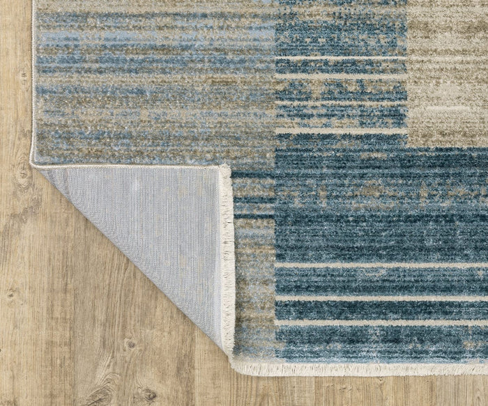 The Oriental Weavers Bauer / 90B Rug, featuring a blue and beige pattern and power-loomed for durability, lies on a light wood floor. One corner of the rug is flipped over, revealing its light gray underside and white fringe along the edge.