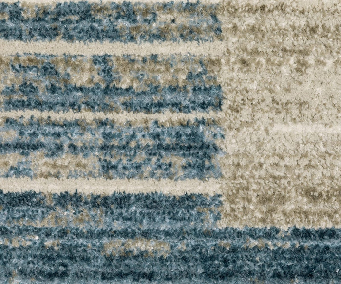 A close-up of the Oriental Weavers Bauer / 90B Rug highlights its textured, power-loomed construction from recycled PET yarn, featuring horizontal blue, beige, and cream stripes with a mix of solid and speckled or faded areas—providing a durable and easy-to-clean surface.