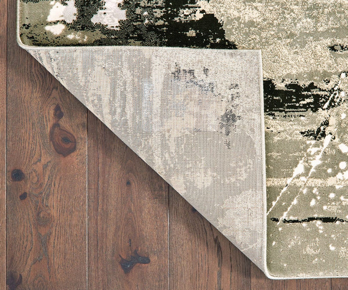 A corner of the Oriental Weavers Bowen / 109E Rug is flipped over, revealing the textured construction of its underside. The patterned, machine-woven rug from the Bowen Collection rests on a brown wooden floor with visible wood grain and knots.