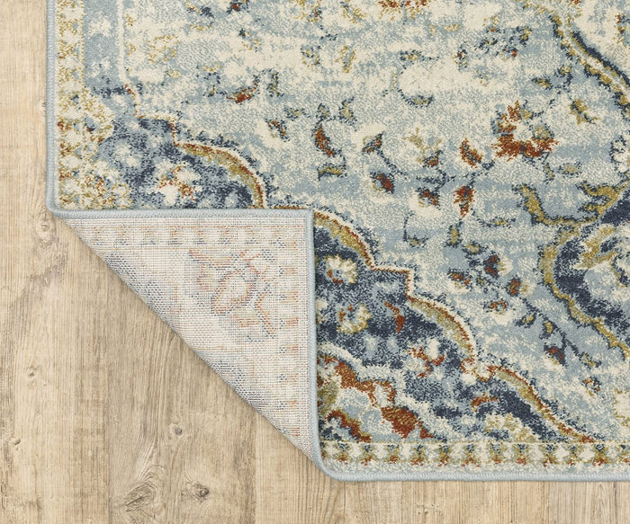 A corner of the Oriental Weavers Branson / BR01A Rug—featuring a blue and beige pattern— is folded over on a light wood floor, showcasing its textured underside and intricate woven design inspired by modern motifs from the Branson Collection.
