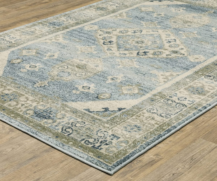 An Oriental Weavers Branson / BR03A Rug, featuring a faded blue, beige, and green geometric pattern with modern motifs and power-loomed for durability, is placed on a light brown wood floor.
