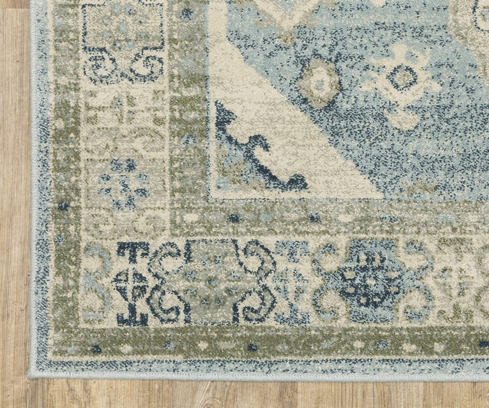 A corner of the Oriental Weavers Branson / BR03A Rug, power-loomed with blue, green, and cream hues, is shown atop a light wood floor. The rug features ornate geometric and floral designs, seamlessly blending timeless elegance with modern motifs.