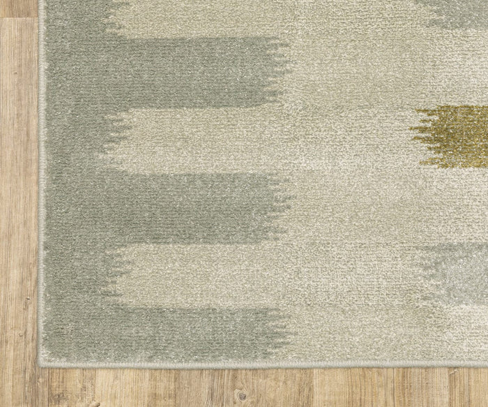 A close-up of the Oriental Weavers Branson / BR09A Rug showcases its modern, abstract pattern in shades of green, beige, and gray, placed on a light wood floor. The rug’s edge is visible on the left side of the image, highlighting its contemporary motifs.