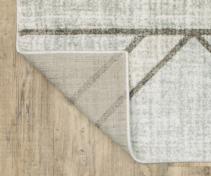 A corner of the Oriental Weavers Cambria / 5569B Rug is flipped over on a wooden floor, revealing both the light gray patterned top design and the textured backing of this high-pile rug crafted from soft polypropylene yarn.