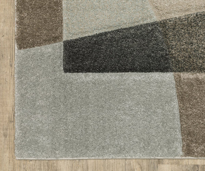 A close-up of the Oriental Weavers Cambria / 84J Rug, a modern high-pile piece from the Cambria Collection, showcasing overlapping geometric motifs in shades of gray, beige, brown, and black on a light wood floor.
