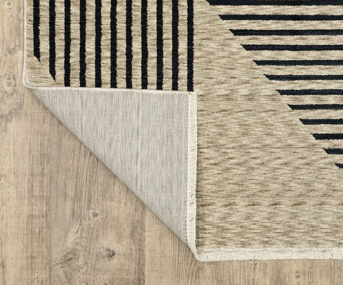 The Oriental Weavers Capella / CAP04 Rug, featuring beige and black stripes with subtle geometric designs, is displayed on a wooden floor with one corner turned over to show the backing, texture, and contemporary style. Made from space-dyed polyester, this rug offers both durability and modern patterning.