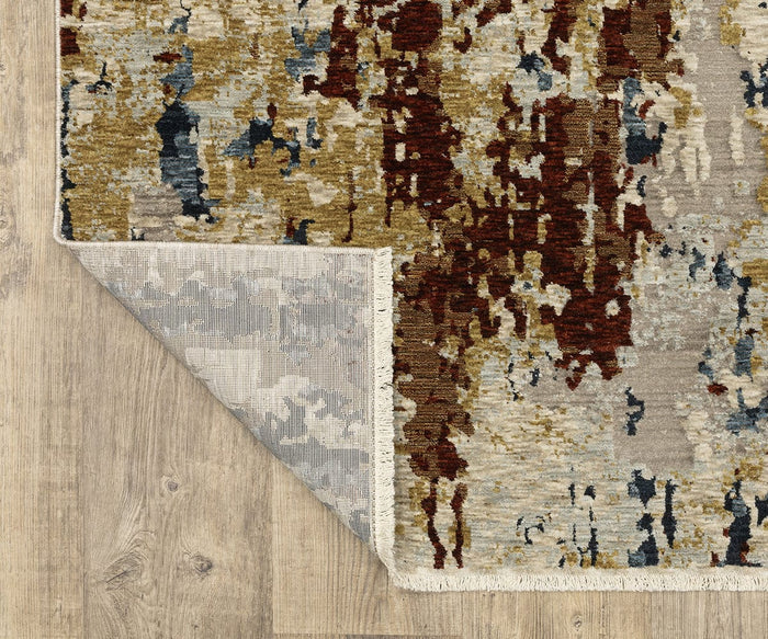 The Oriental Weavers Capella / CAP11 Rug showcases an abstract pattern in shades of brown, gold, blue, and cream atop a wooden floor. Made from space-dyed polyester for enhanced depth and color variation, this rug is pictured with one corner flipped to display its gray and white underside.