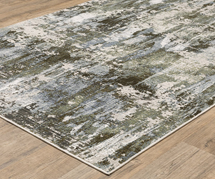 The Oriental Weavers Caravan / 2060F Rug, crafted from space-dyed polyester and featuring an abstract, nature-inspired pattern in green, blue, gray, and cream tones, rests on a light wood floor. This rug showcases a modern distressed design with beautifully uneven color blending.