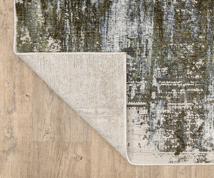 A corner of the Oriental Weavers Caravan / 2060F Rug is flipped over, revealing the underside, on a light wood floor. Part of the Caravan Collection, this rug features a nature-inspired pattern in abstract green, blue, and beige designs, beautifully crafted with space-dyed polyester for added depth and texture.