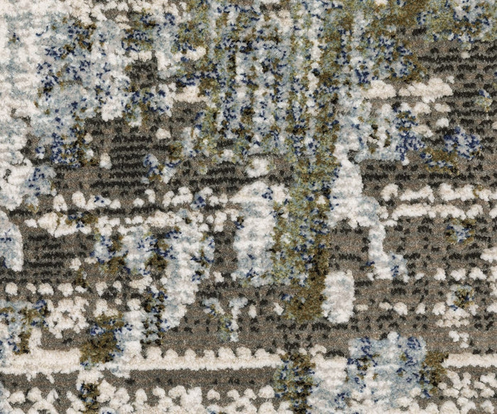 Close-up of the Oriental Weavers Caravan / 2060F Rug, featuring a nature-inspired pattern with abstract, mottled shapes in shades of gray, white, blue, and olive green. Expertly crafted from space-dyed polyester, this textured carpet design resembles paint splatters or uneven organic forms.